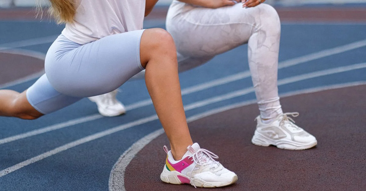Deux femmes en vêtements de sport effectuant des fentes en plein air sur une piste.