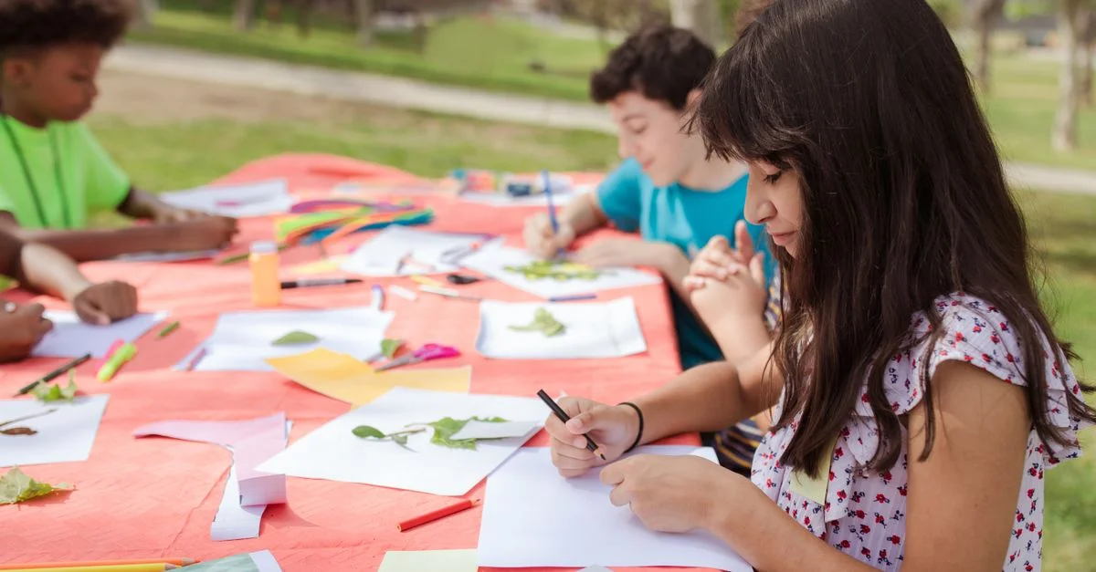 Des enfants participant à des activités artistiques en plein air, créant des œuvres et des dessins par une journée ensoleillée.