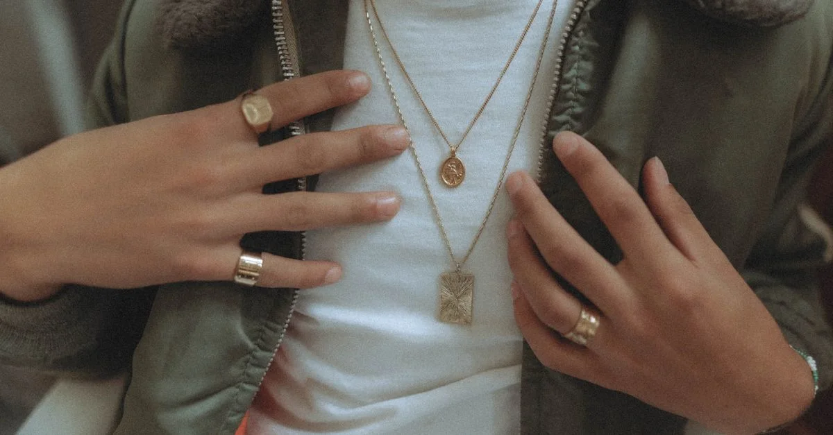 Gros plan sur des mains élégantes mettant en valeur des bagues et des colliers en or, soulignant le style de mode.