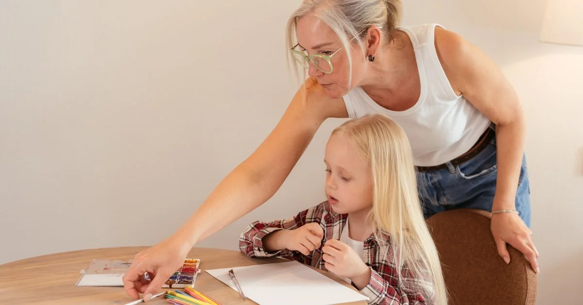 Une grand-mère enseignant à sa petite-fille à dessiner autour d'une table en bois à l'intérieur. Moment créatif en famille.