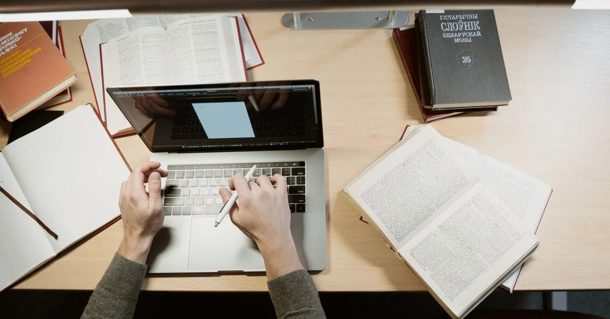 Un étudiant étudie avec un ordinateur portable et des livres, mettant en avant un environnement d'apprentissage.