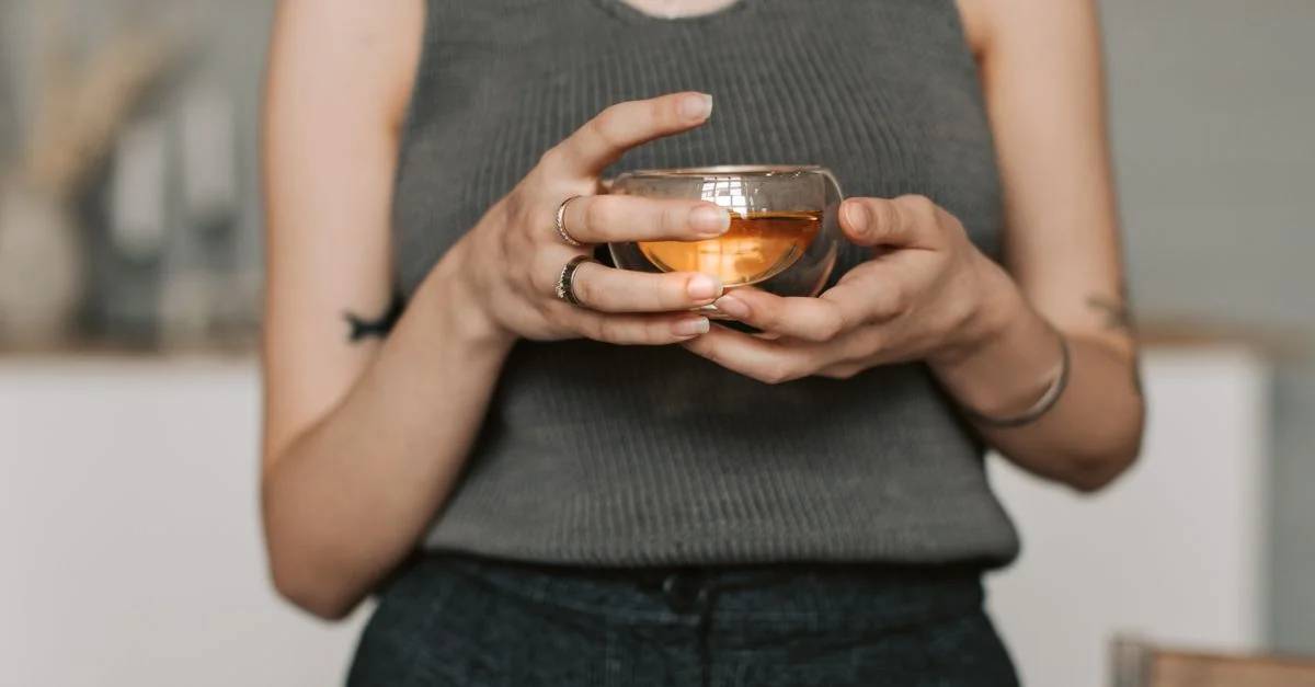 Une personne en débardeur gris savourant une tisane chaude à l'intérieur. Parfaites images de mode de vie serein.