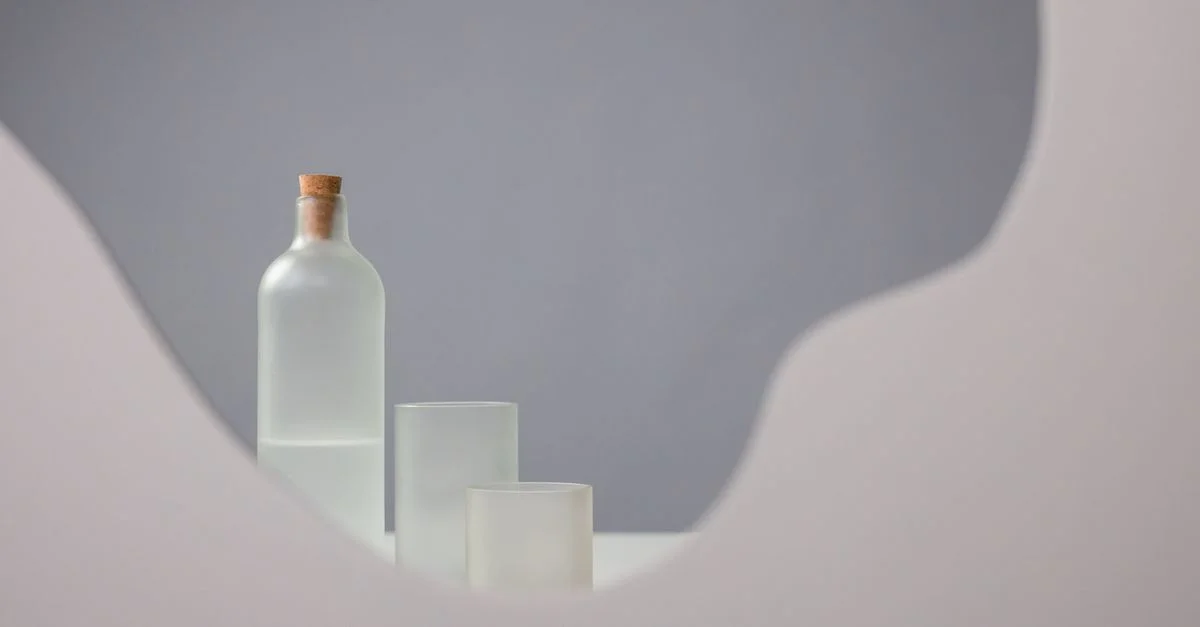 Nature morte esthétique mettant en vedette une bouteille en verre dépoli et des tasse contre un fond doux.