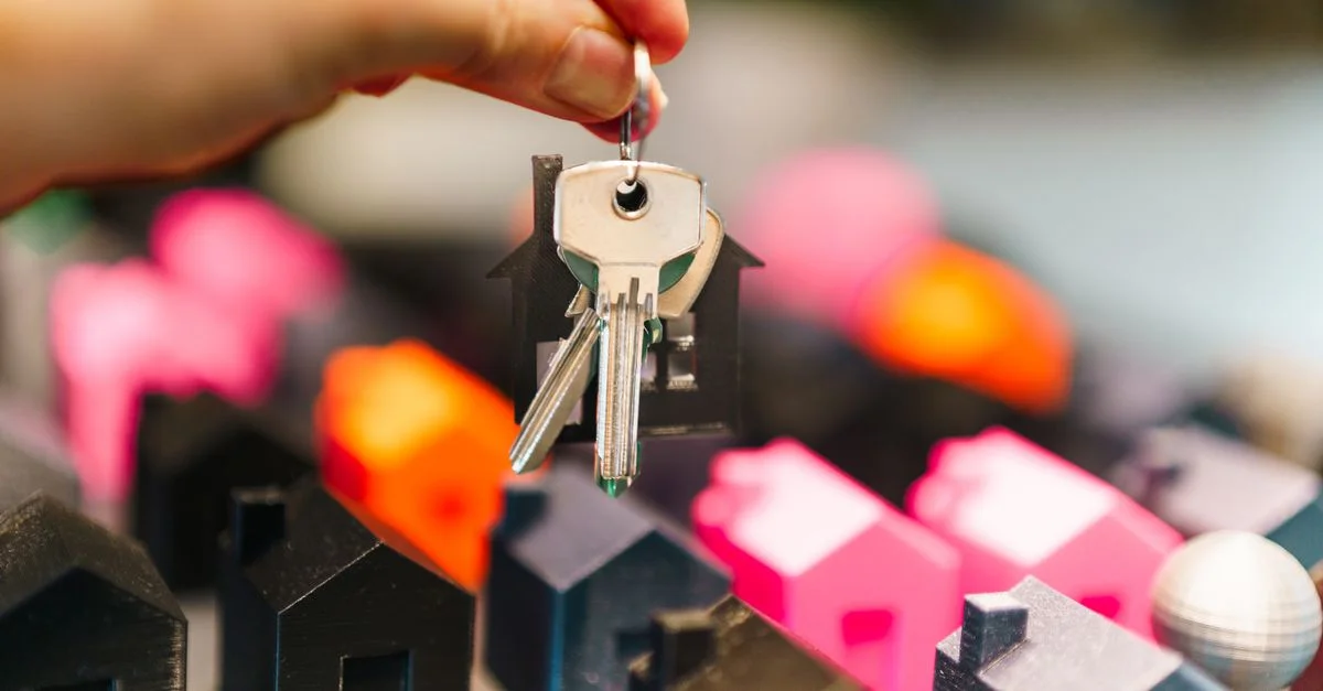 Des maisons miniatures colorées et une main tenant des clés représentant des décisions immobilières.