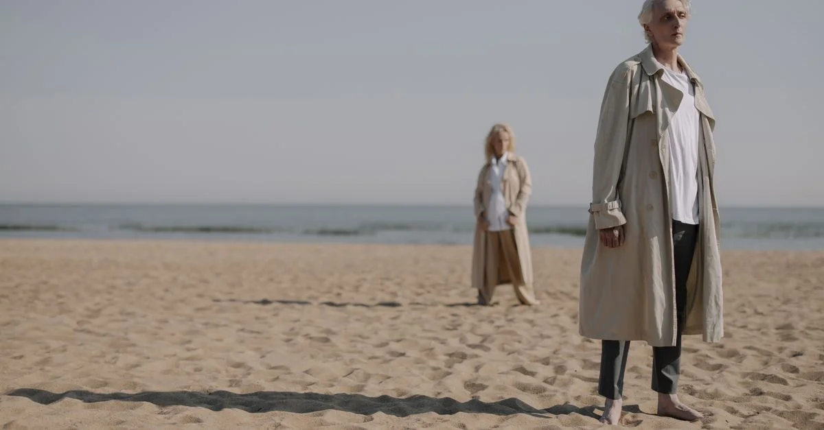 Un couple âgé profitant d'une journée d'été à la plage dans des trenchs stylés, capturant un moment serein et romantique.