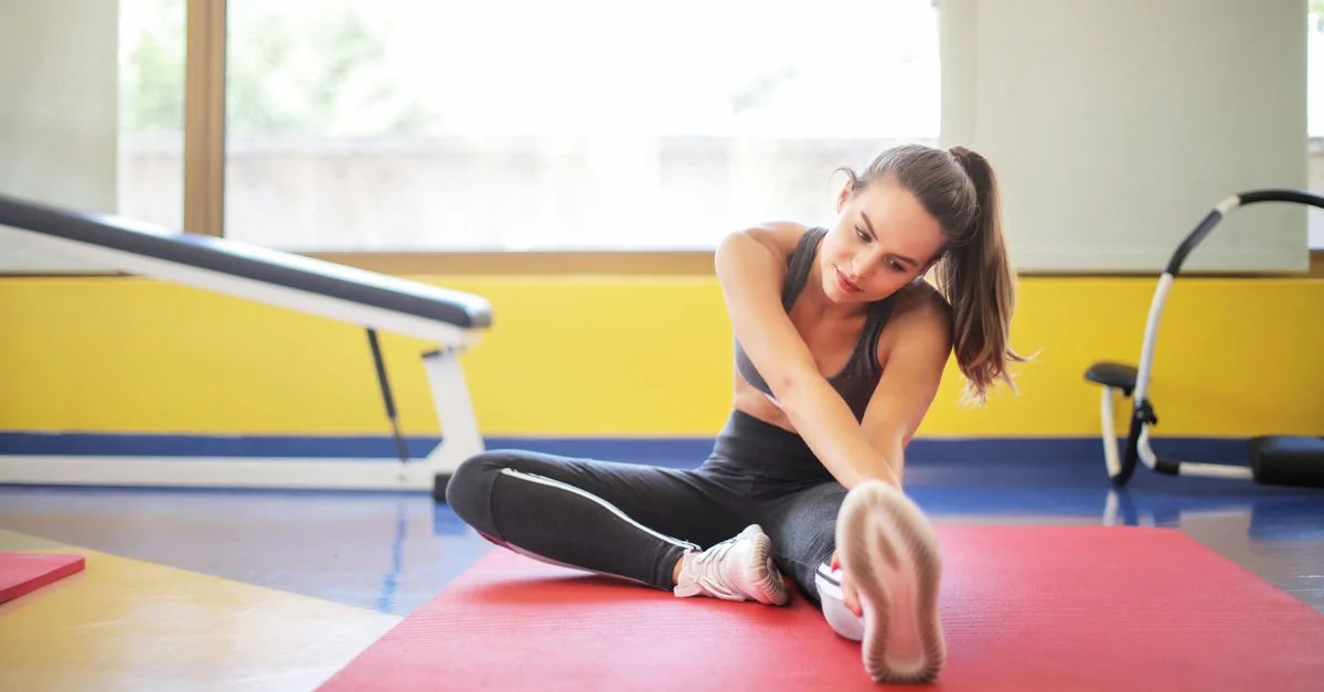 Athlète féminine s'étirant sur un tapis de yoga rouge à l'intérieur, mettant en avant la flexibilité et la forme physique.
