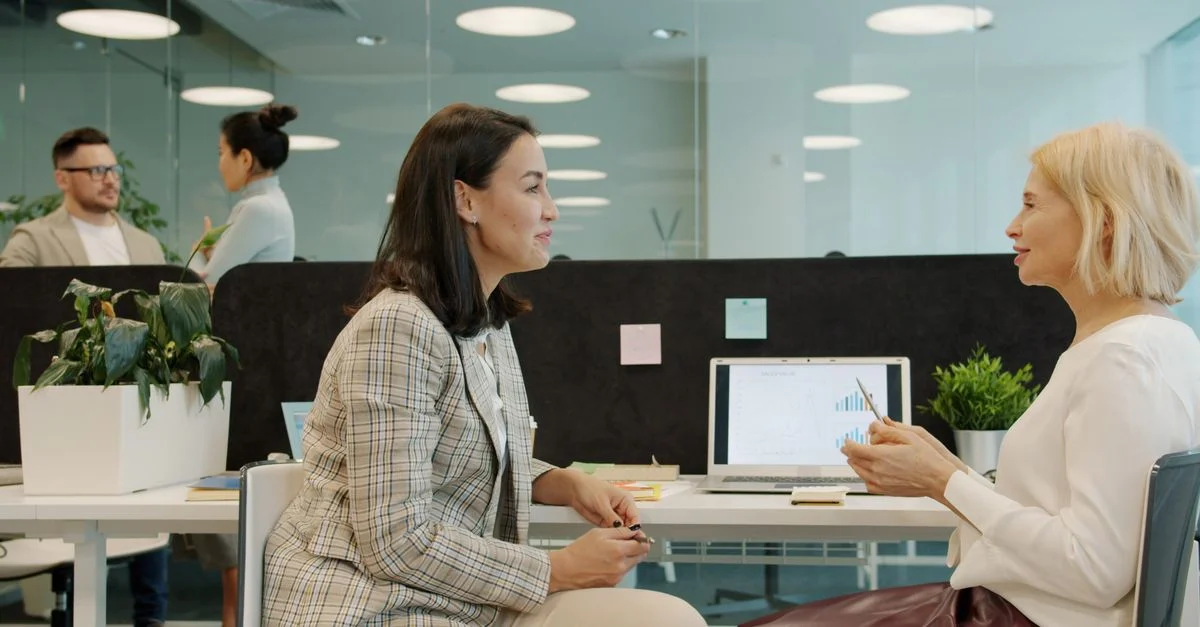 Deux femmes discutent affaires dans un bureau moderne.