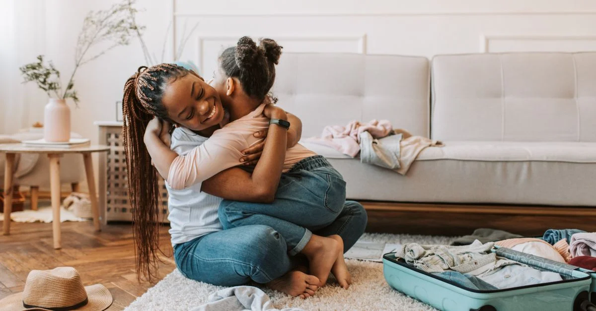 Une mère et sa fille partagent une étreinte affectueuse en préparant un voyage avec une valise ouverte à la maison.